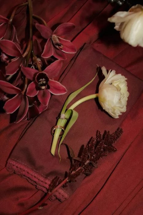 Wedding rings placed on a tulip stem among burgundy orchids and silk fabric styling details at Common Goods.