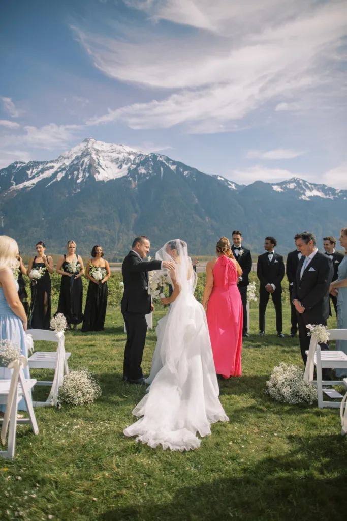 Bride walking down aisle with guests and wedding party gathered outdoors at Fraser River Lodge