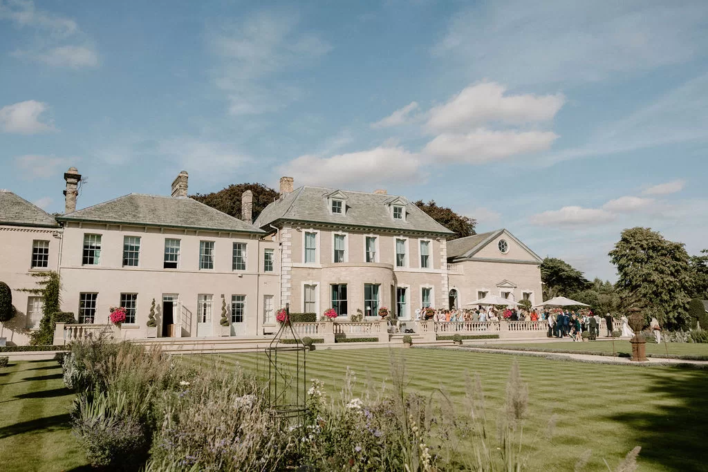 Exterior view of Hotham Hall Estate with guests gathered on terrace and gardens