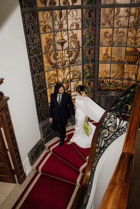 Newlyweds walking down the red carpet staircase together inside the historic Infante Sagres hotel.