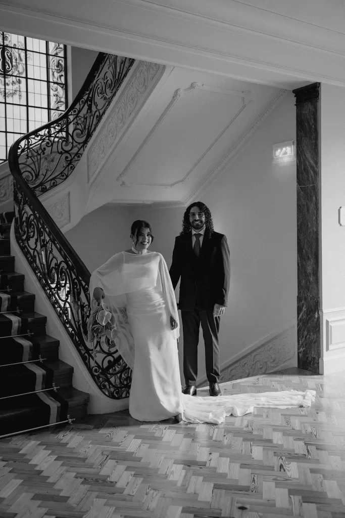 Bride and groom posing together beside the sweeping staircase inside the historic Infante Sagres hotel.