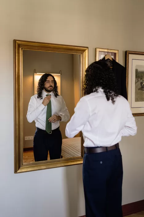 Groom adjusting his green tie in a mirror while getting ready for the wedding at Infante Sagres hotel.