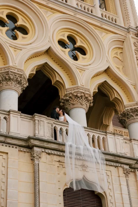 Bride and groom kiss on ornate balcony at Isola del Garda with flowing veil and intricate architecture