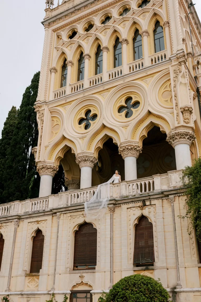 Bride on balcony with flowing veil against ornate Isola del Garda facade