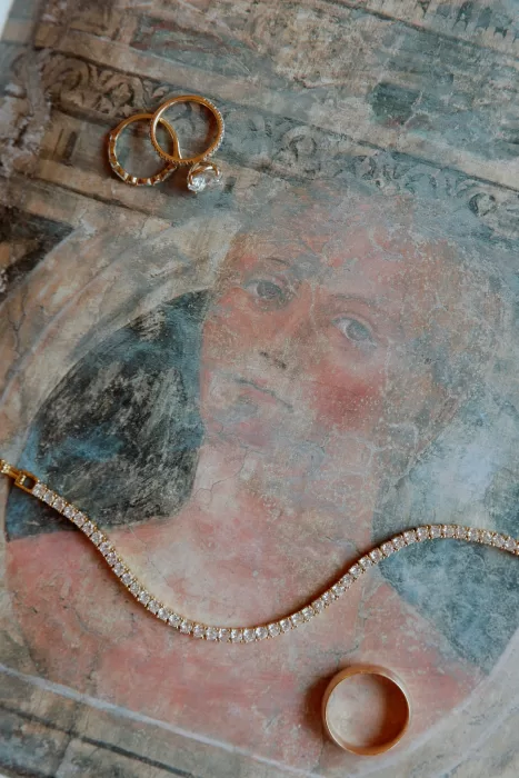 Wedding rings and diamond necklace placed on aged fresco artwork at Isola del Garda