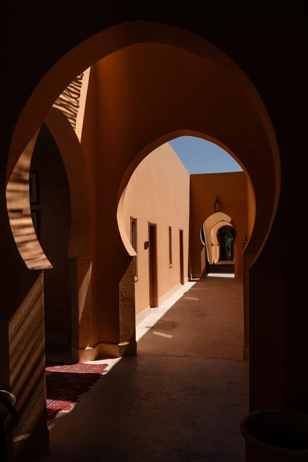 Sunlit corridor framed by Moorish arches and terracotta tones at Jnane Tamsna.