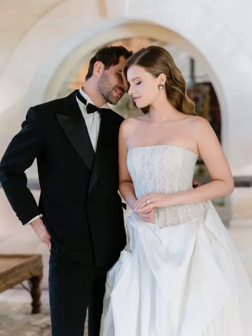 Bride and groom in black tie standing closely together beneath an arched doorway inside Mas de Chabran.