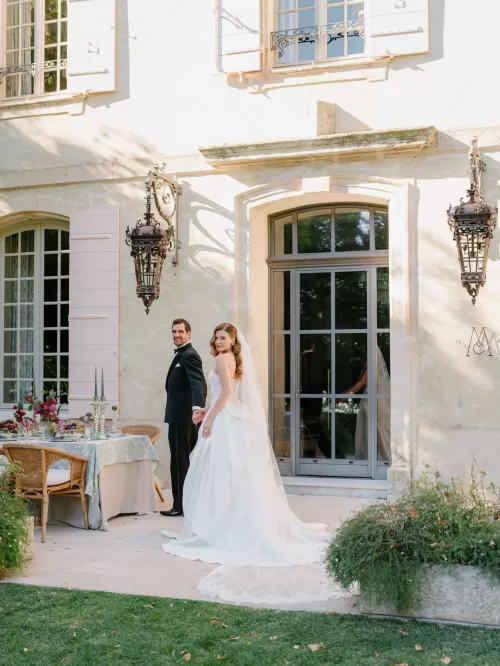 Bride and groom holding hands outside the elegant facade of Mas de Chabran beside a styled reception table.