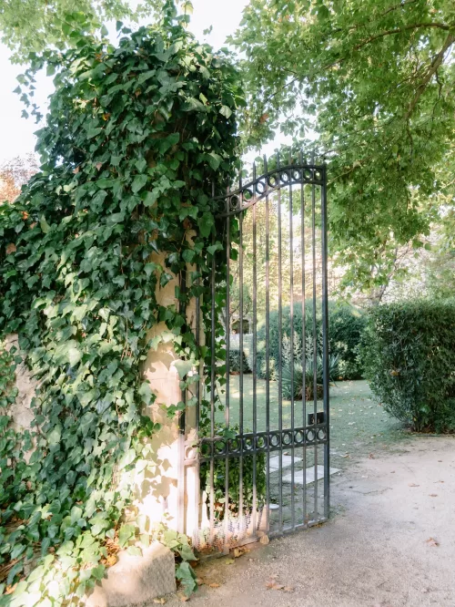 Ivy-covered stone pillar and wrought iron garden gate opening into the leafy grounds of Mas de Chabran.