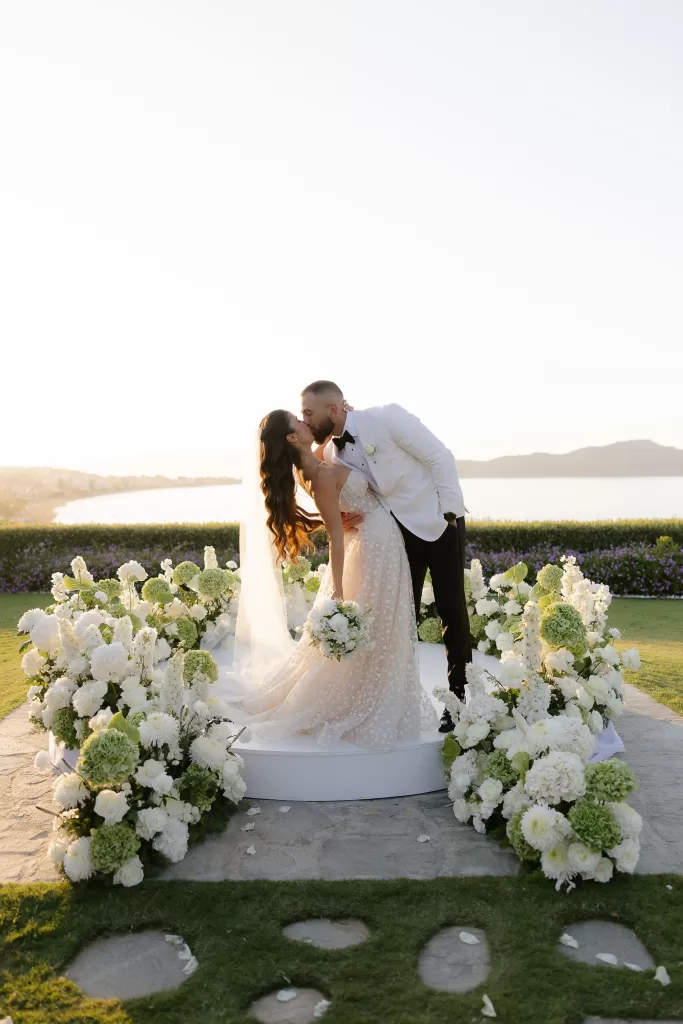 Newlyweds sharing a kiss at Sea View by En Kipo surrounded by white flowers with soft golden light and sea views