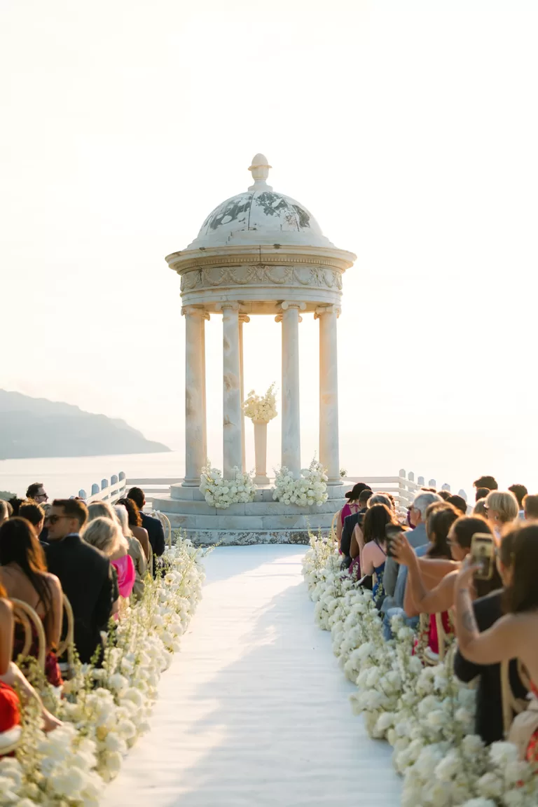 Guests seated along a flower-lined aisle during a ceremony at Son Marroig overlooking the Mediterranean