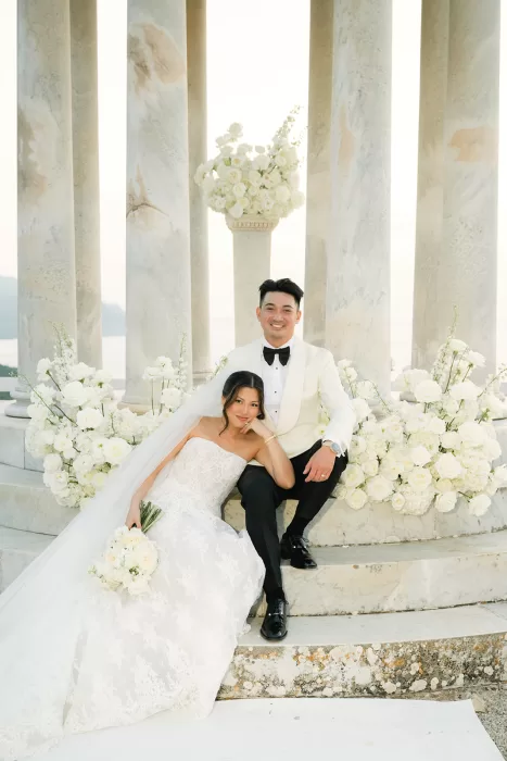 Bride and groom seated at the temple steps at Son Marroig surrounded by white floral arrangements