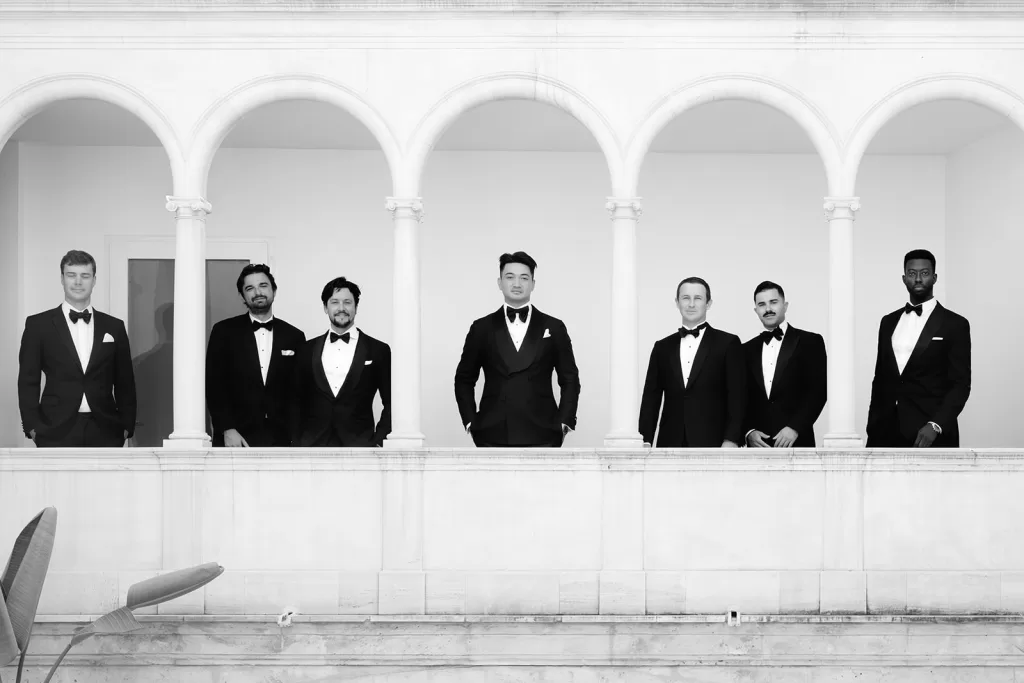 Groom and groomsmen in black tuxedos standing beneath white arches at Son Marroig