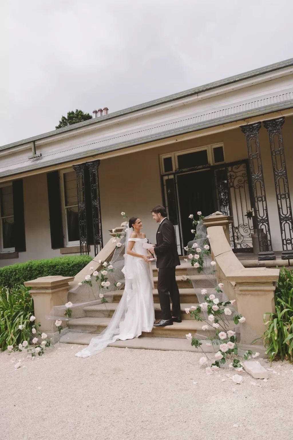Bride and groom holding hands on the rose-decorated staircase at Wallalong House.