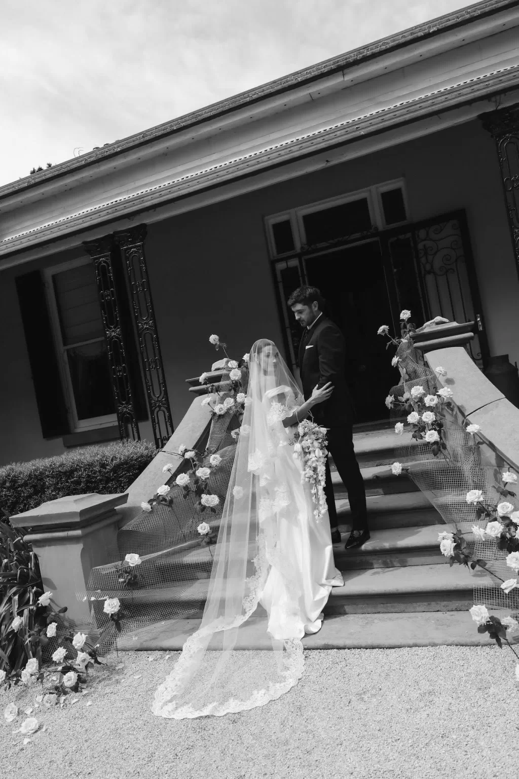 Bride and groom holding hands on the rose-decorated staircase at Wallalong House.