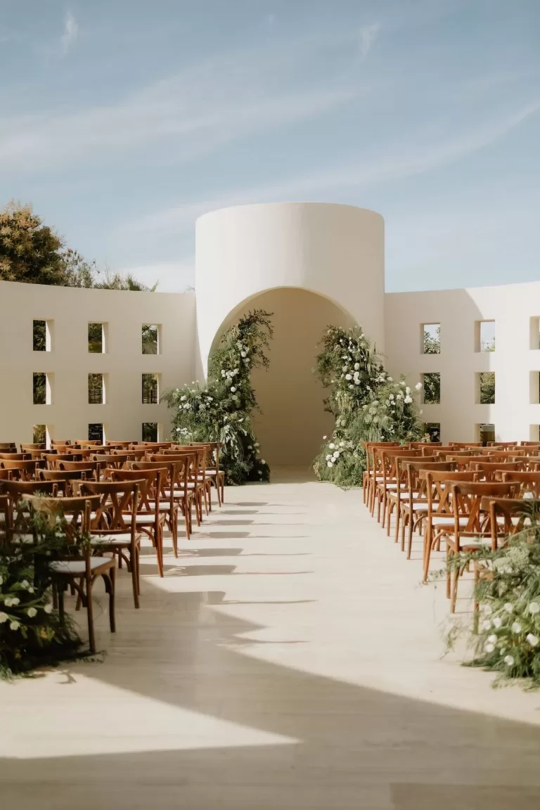 Sunlit wedding ceremony at Baja Luna with a modern white arch and lush green floral arrangements.
