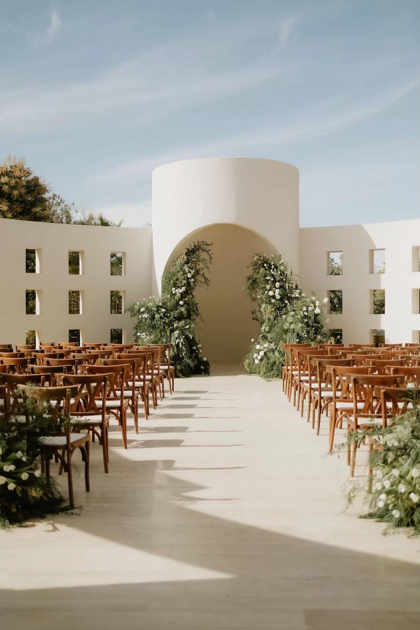 Sunlit wedding ceremony at Baja Luna with a modern white arch and lush green floral arrangements.