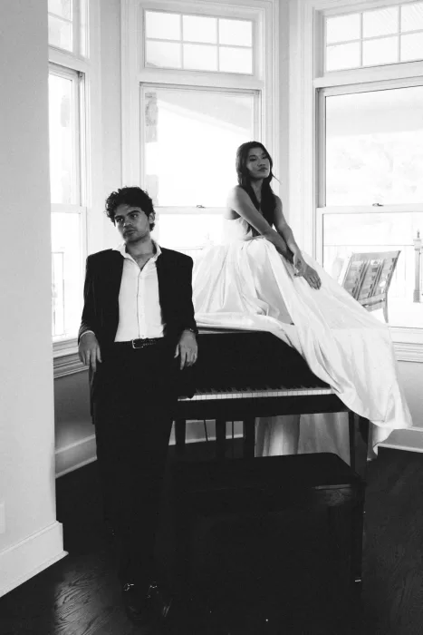 Black and white portrait of the couple seated around a grand piano.