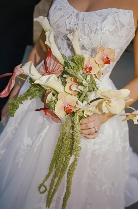 Bride holding sculptural bouquet of orchids, calla lilies and trailing greenery