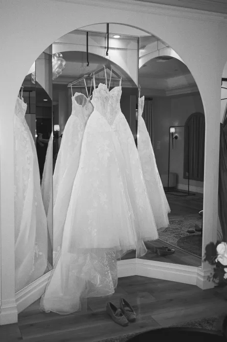 Bridal gown hangs in front of arched mirrors before the wedding