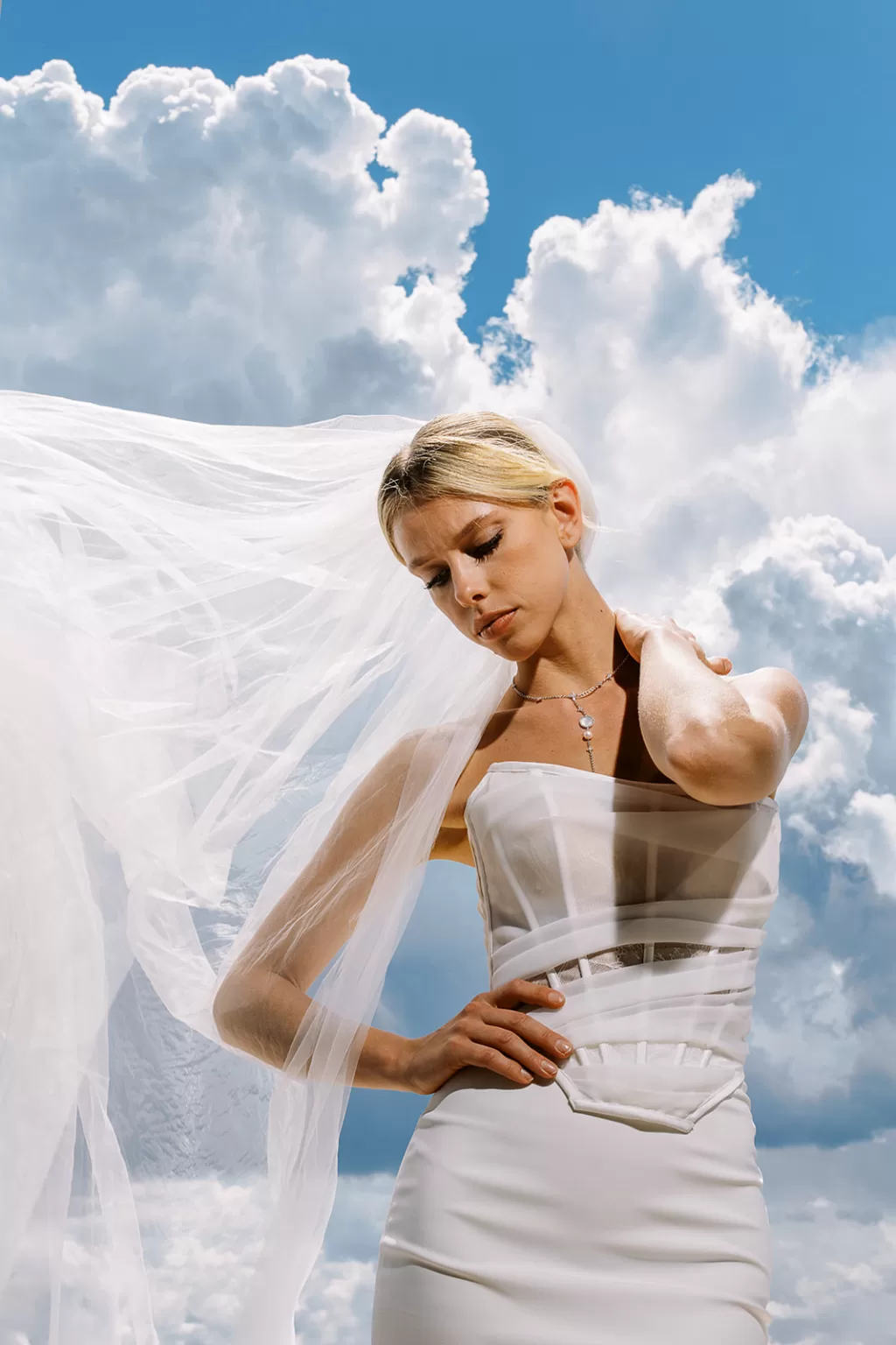 bride in structured gown with flowing veil against bright sky and clouds