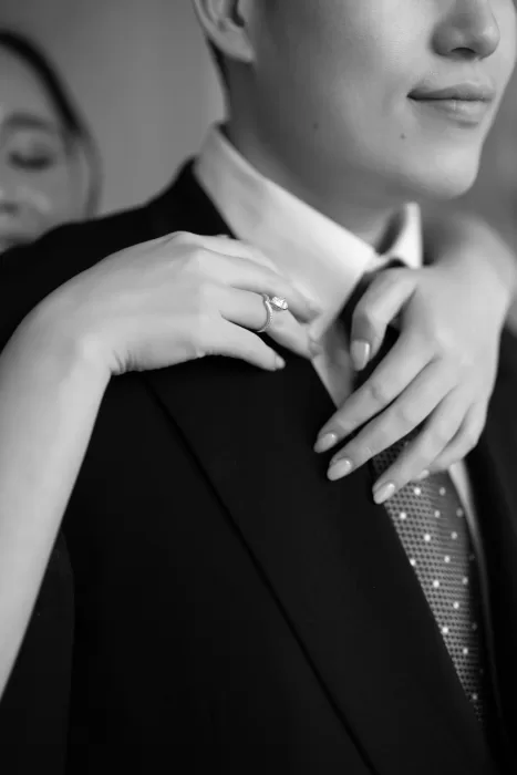 Close-up of bride’s engagement ring and hands resting on groom’s suit