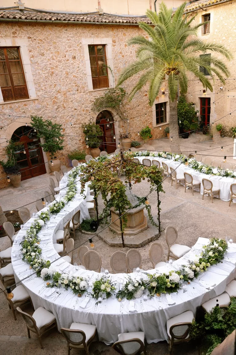 Elegant courtyard reception at Cases de Sa Fonseca with long U-shaped table decorated with white flowers and greenery.