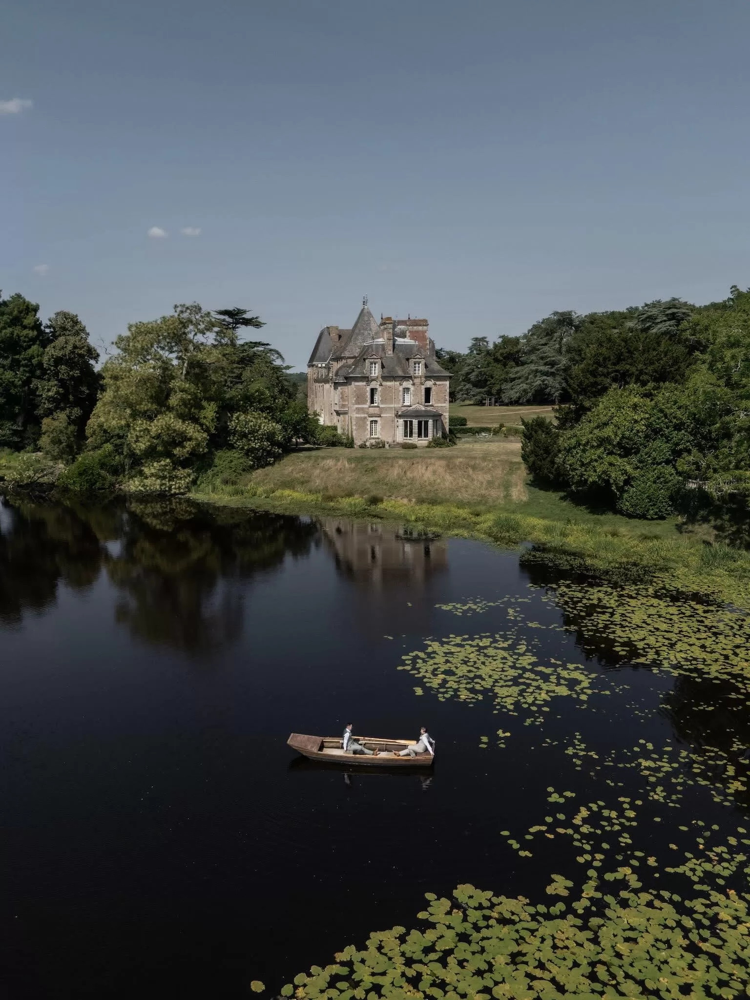 The grooms in a wooden rowboat on the tranquil lake beside Château de Pordor surrounded by lily pads.