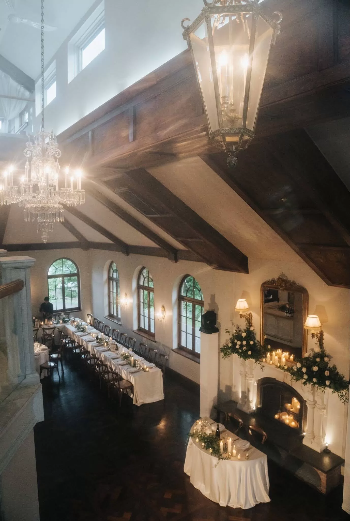 Elegant indoor reception setup at Château Ste. Agnès with long tables, chandeliers, and a floral-covered fireplace.