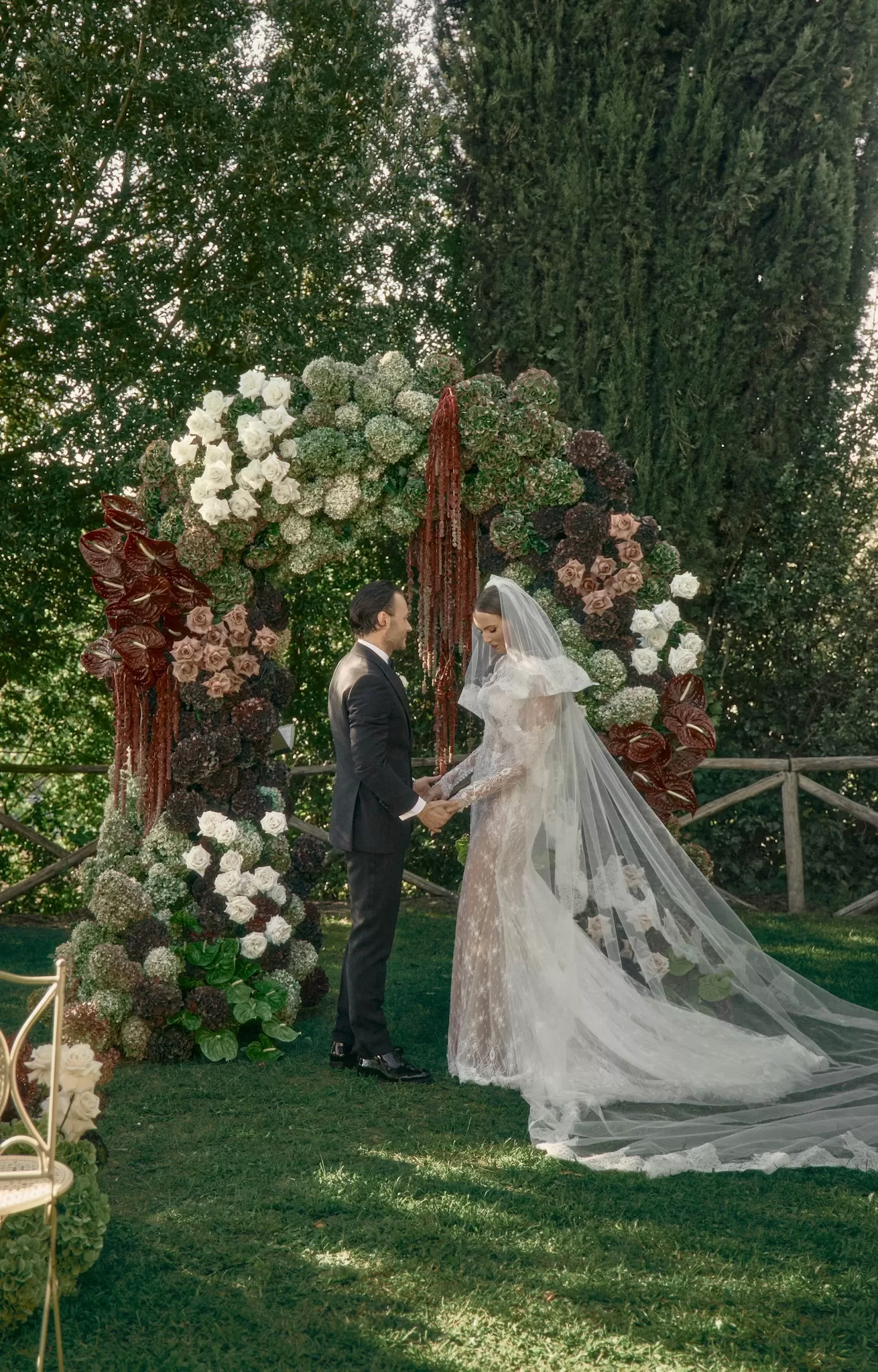 Bride and groom standing beneath dramatic floral ceremony arch