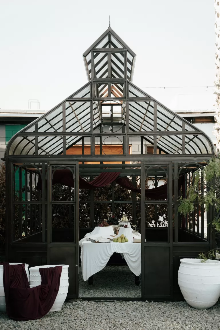 Glass greenhouse reception space at Comman Goods set with a draped table and styled wedding décor.