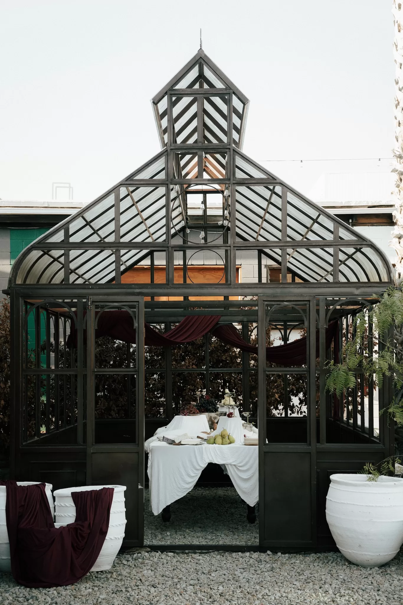 Glass greenhouse reception space at Comman Goods set with a draped table and styled wedding décor.