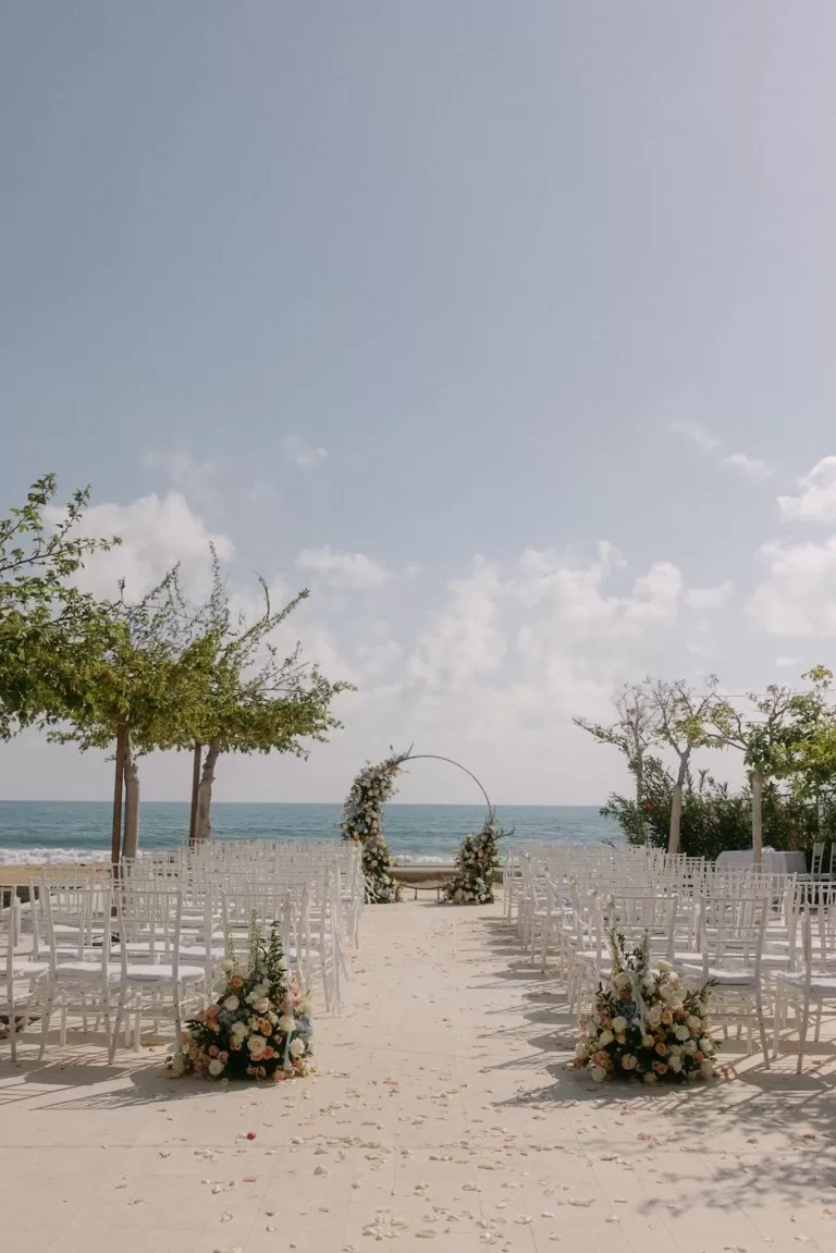 Elegant seaside ceremony setup with floral arch and white chairs at Coral Residences.