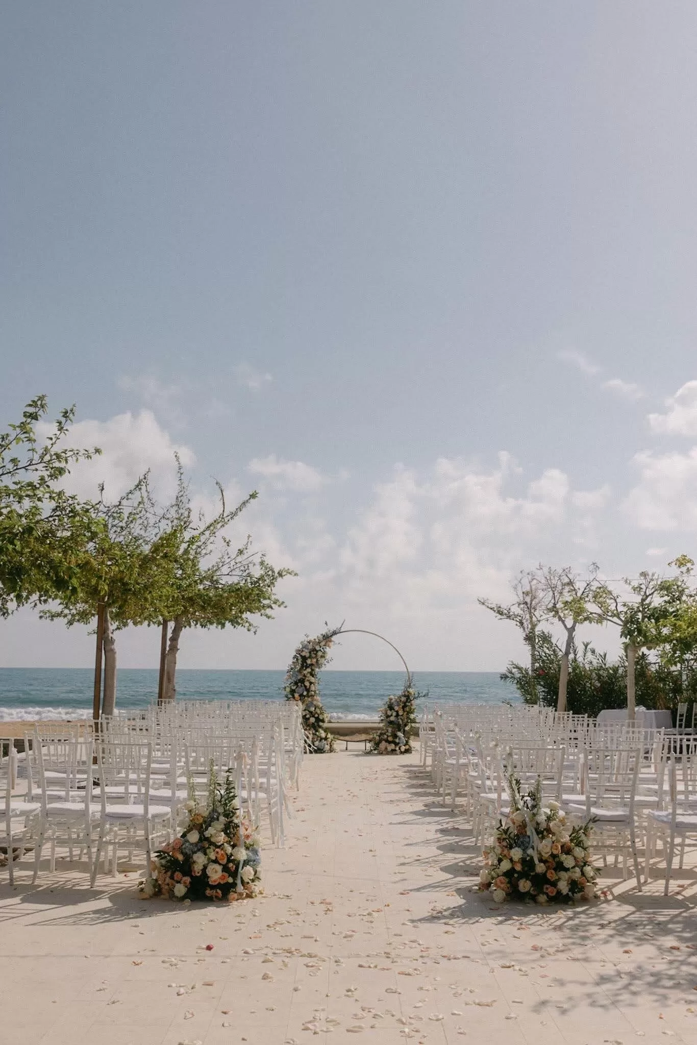 Elegant seaside ceremony setup with floral arch and white chairs at Coral Residences.