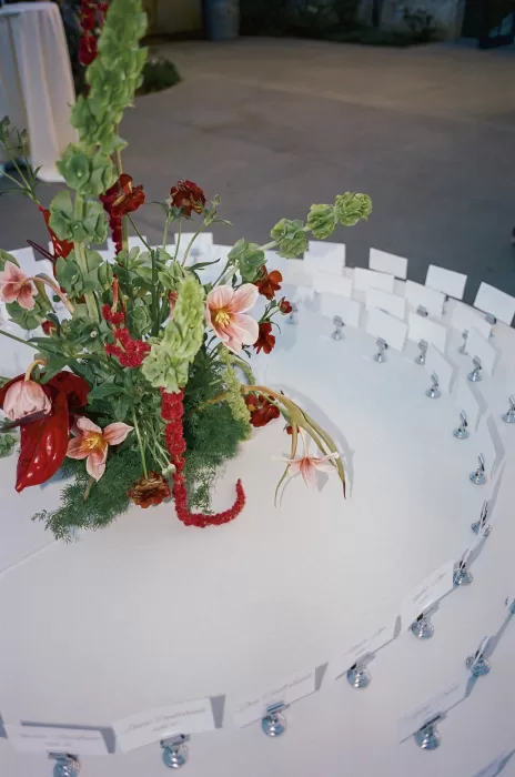Close-up of escort cards circling a modern red and green floral arrangement