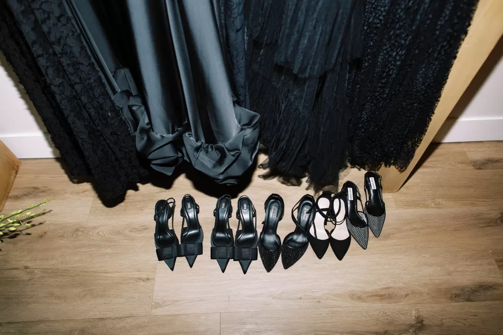 Black bridesmaid shoes lined up beneath dresses during wedding preparations