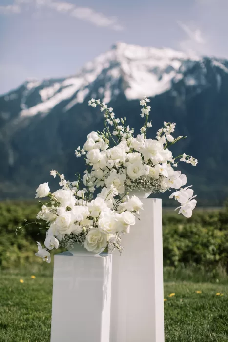 White floral arrangement on pedestal with mountain backdrop at Fraser River Lodge ceremony