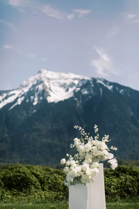 White floral arrangements on plinths with mountain backdrop at Fraser River Lodge