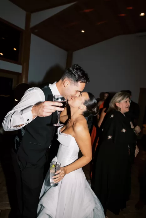 Bride and groom kissing on dance floor holding drinks during reception at Fraser River Lodge