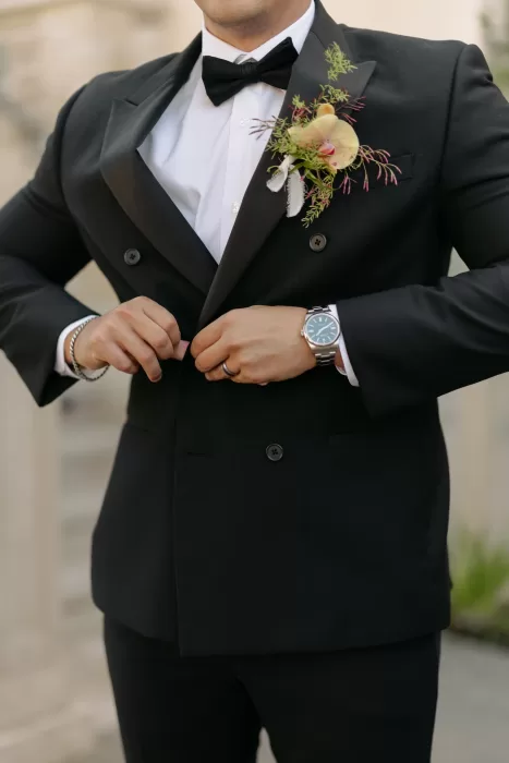 Groom adjusts tailored black tuxedo with soft floral boutonniere and classic bow tie