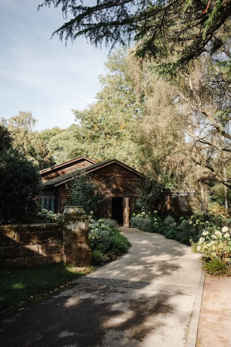 Path leading to Hampton Manor’s rustic barn surrounded by lush trees and blooming hydrangeas.