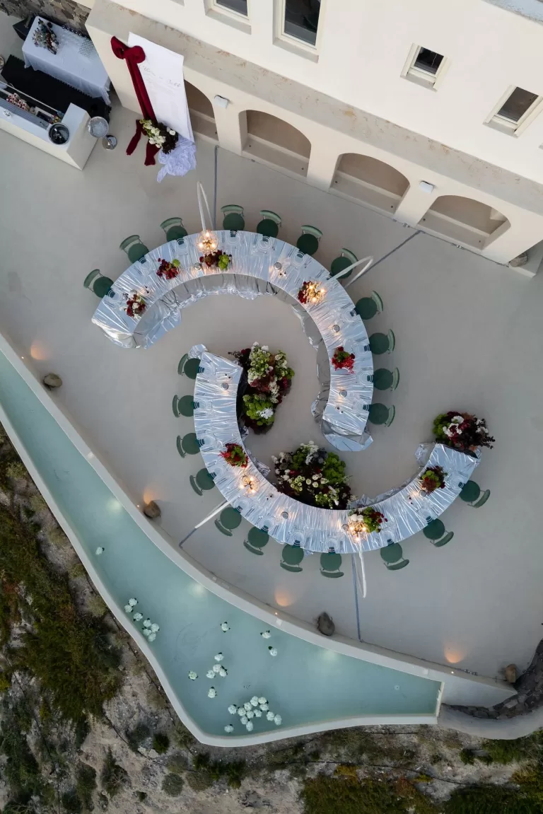 Overhead view of a curved wedding reception layout with floral installations and water features at Islet Santorini.
