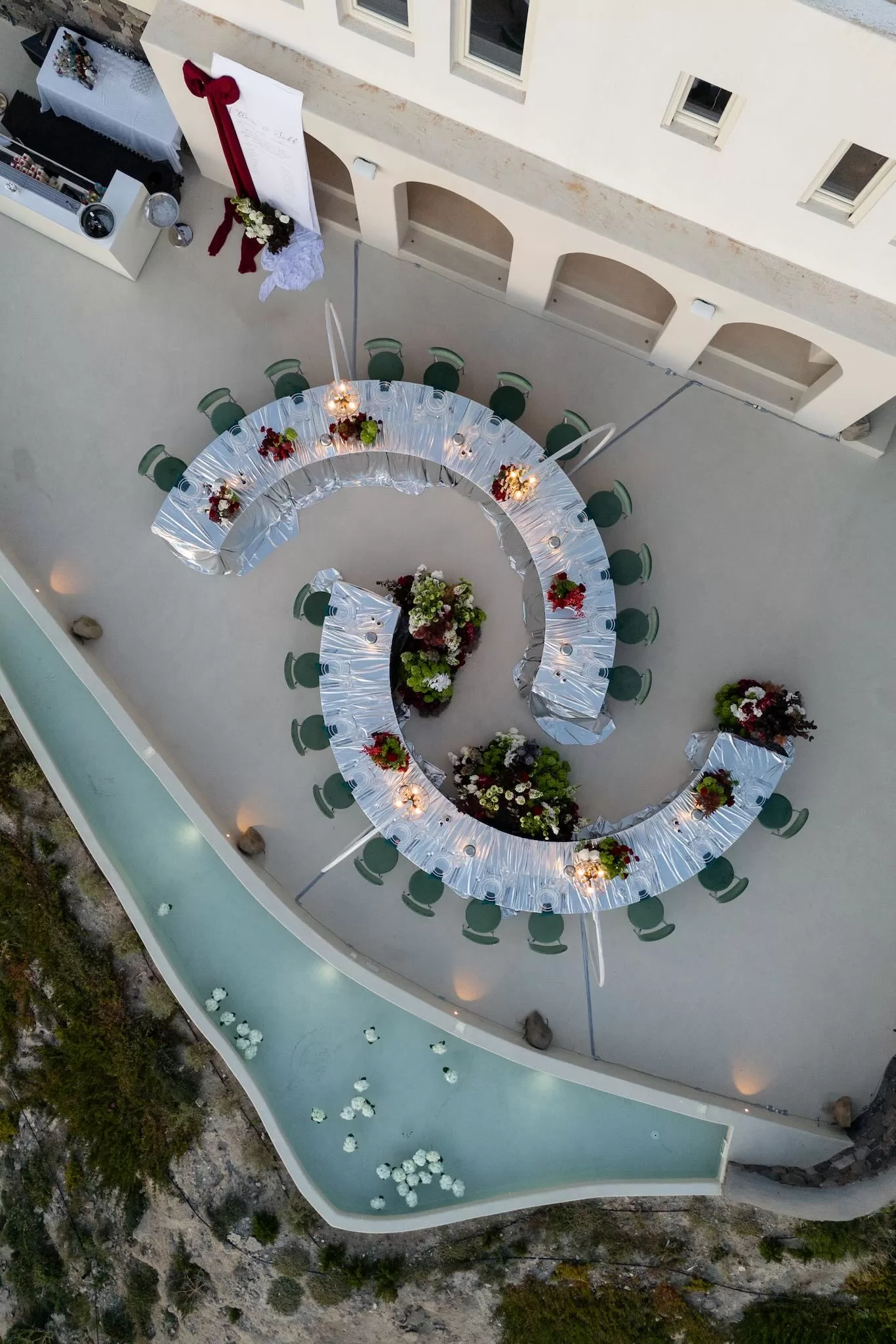 Overhead view of a curved wedding reception layout with floral installations and water features at Islet Santorini.