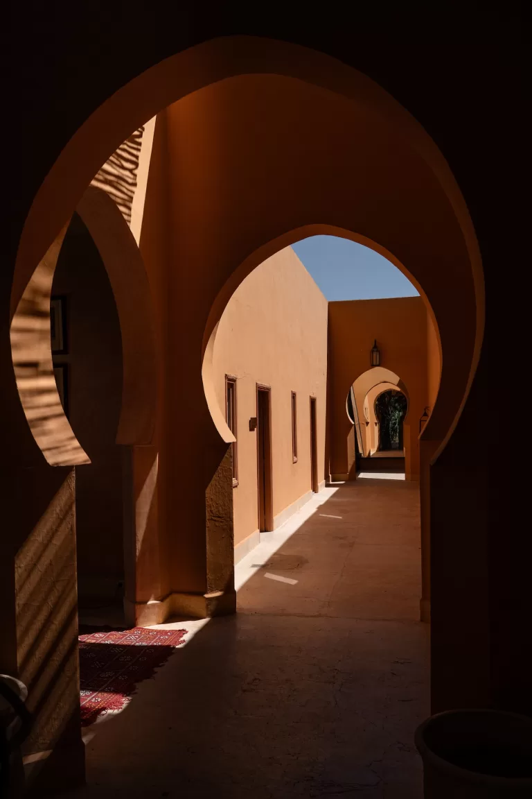 Sunlit corridor framed by Moorish arches and terracotta tones at Jnane Tamsna.