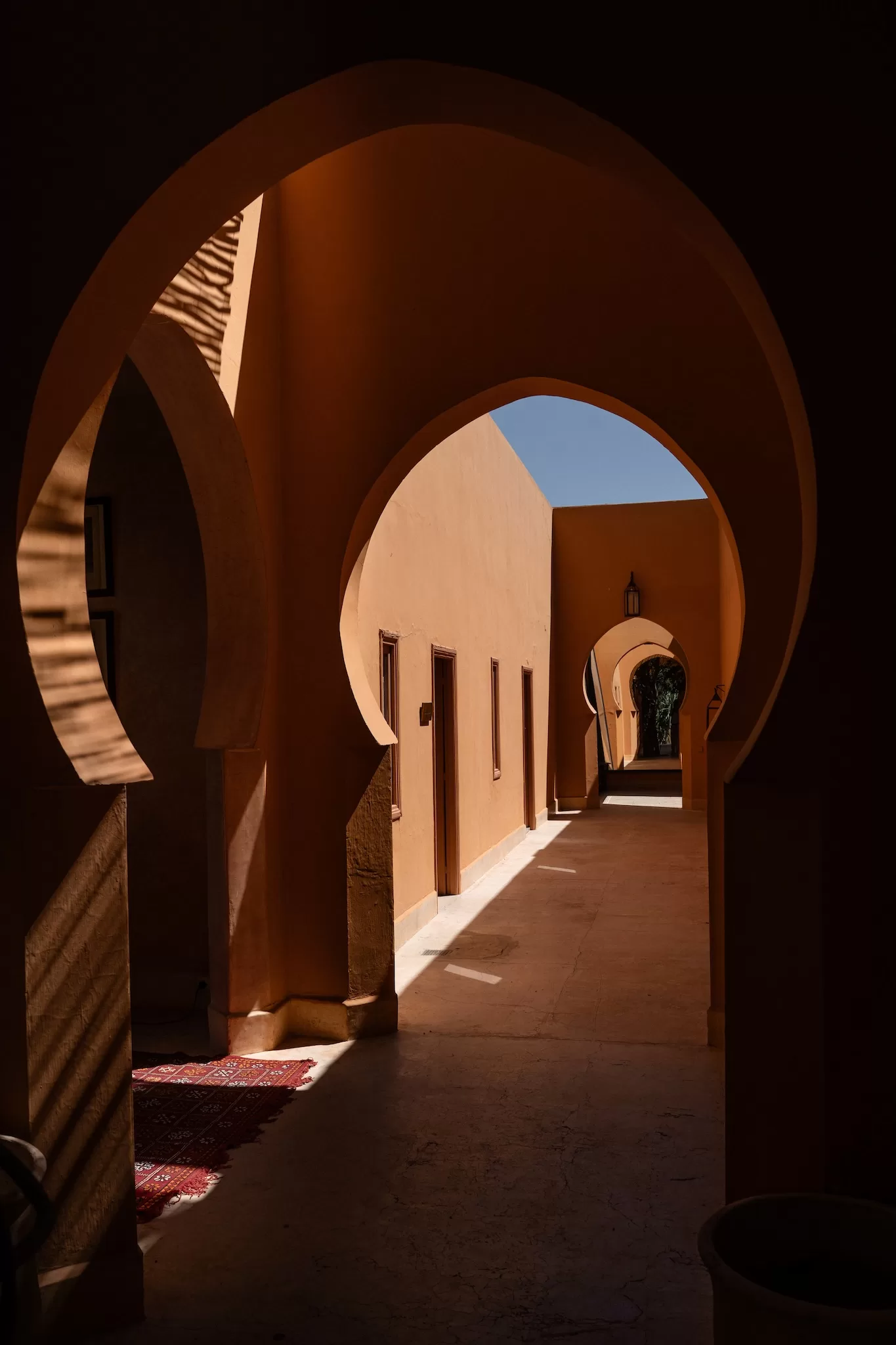 Sunlit corridor framed by Moorish arches and terracotta tones at Jnane Tamsna.