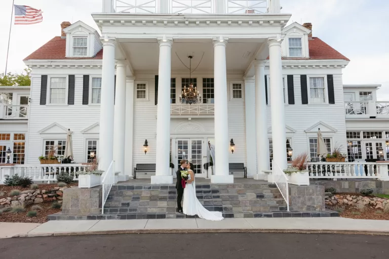 Couple kissing in front of The Manor House in Colorado with its grand white facade behind them.