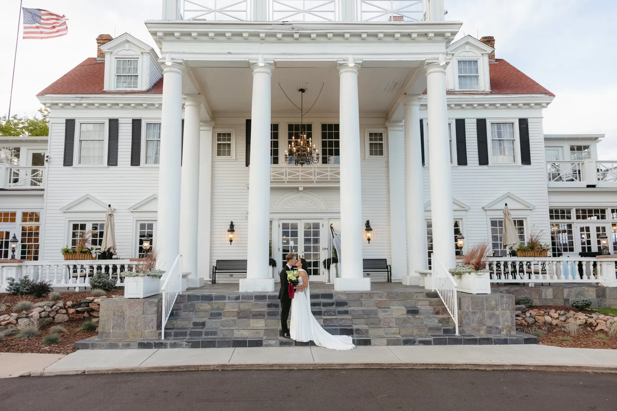 Couple kissing in front of The Manor House in Colorado with its grand white facade behind them.