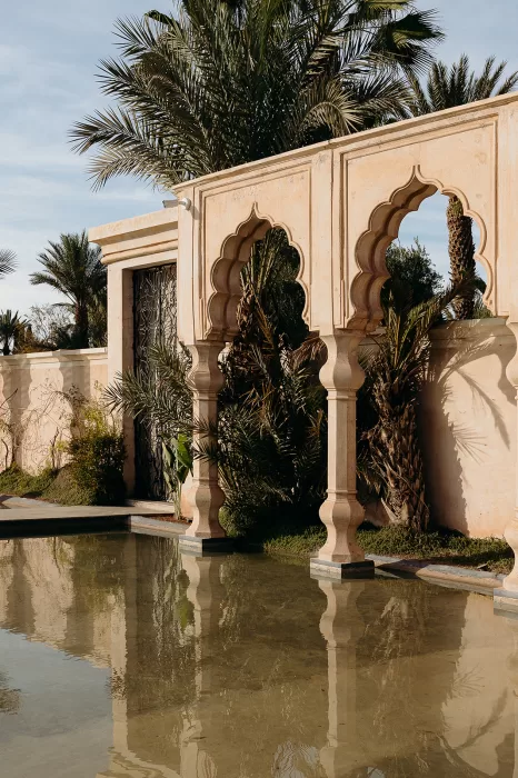 Ornate arches reflected in still water with palm trees at Palais Namaskar
