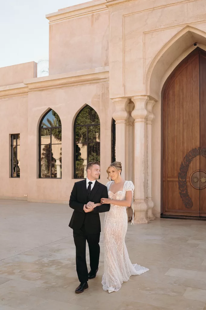 Bride and groom walking together through sunlit courtyard with arches at Palais Namaskar
