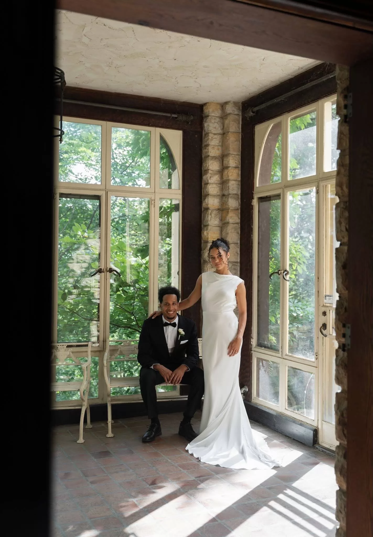 Bride and groom pose elegantly in the bright sunroom framed by arched windows at The Plummer House.